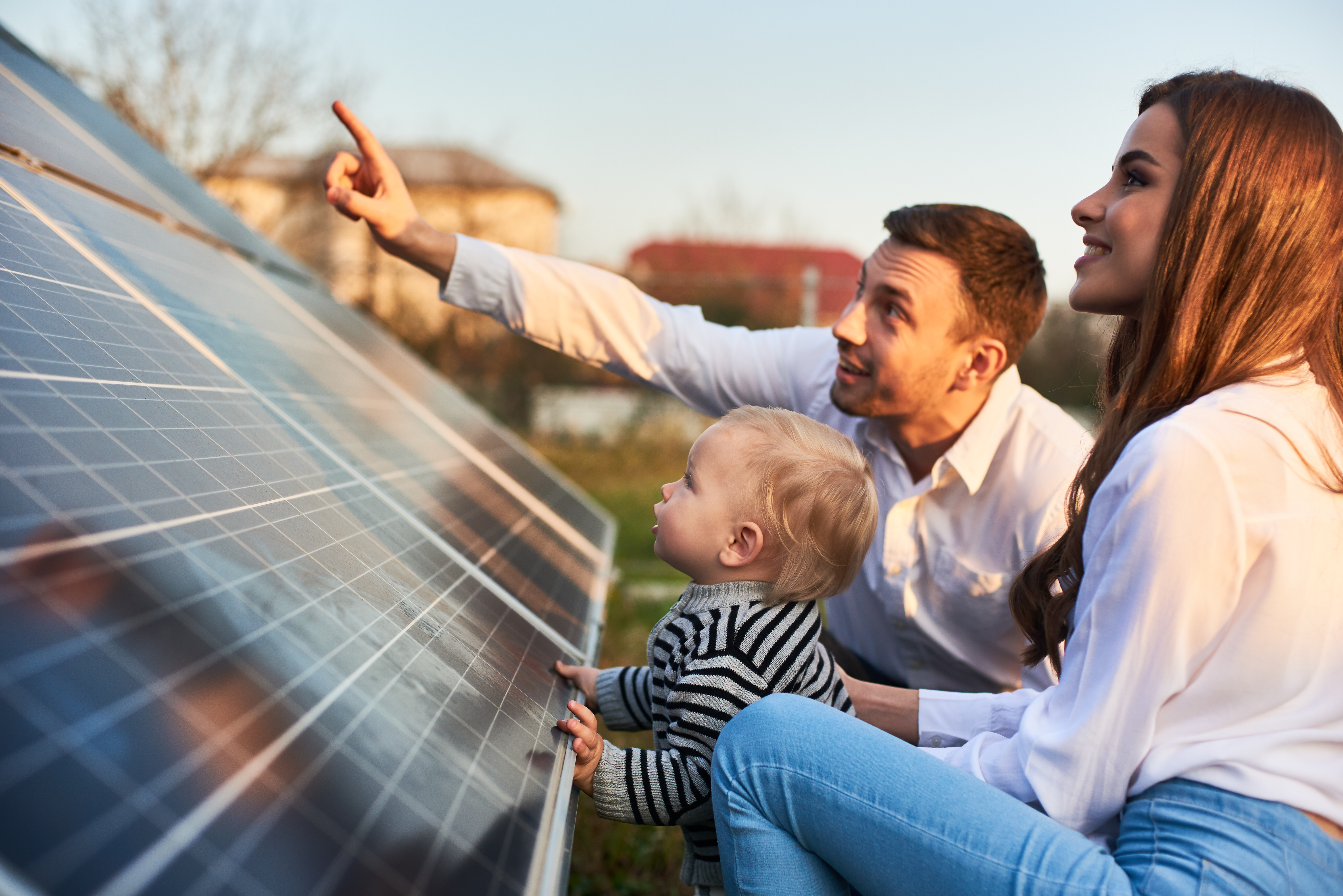 Man shows his family the solar panels on the plot near the house during a warm day